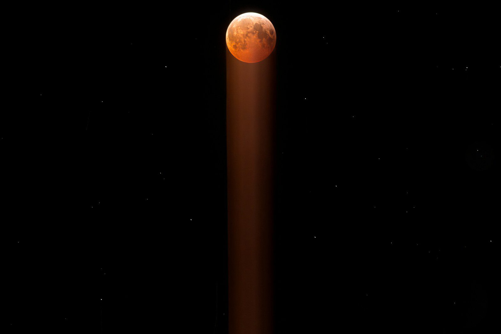 Blood moon in starry night sky with light beam