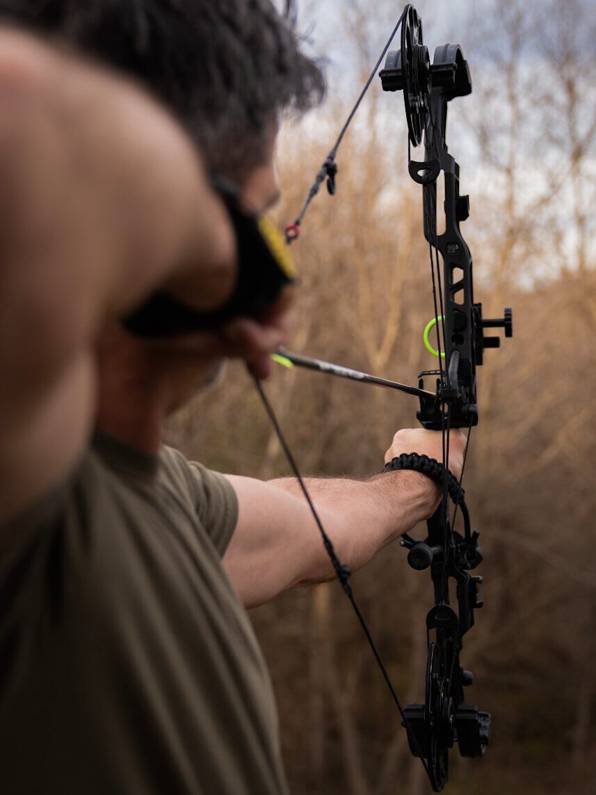 Man aiming a compound bow and arrow outdoors